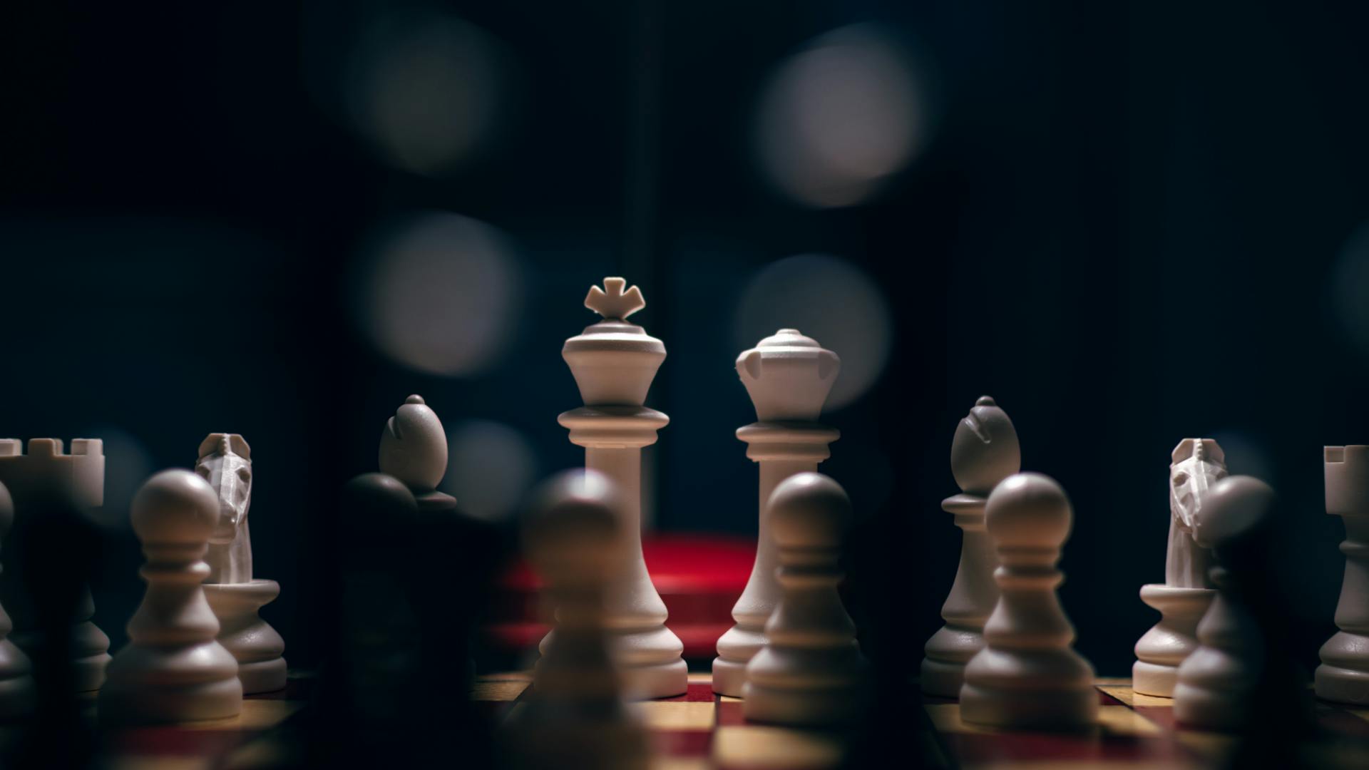 Close-up of a chessboard in low light, focusing on white chess pieces, capturing an intense game moment.